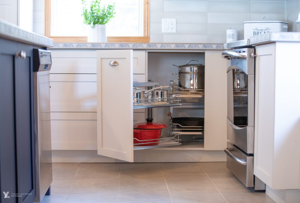 Rangement de cuisine sur mesure avec mécanismes coulissants permettant d’optimiser l’espace dans les armoires de coin.